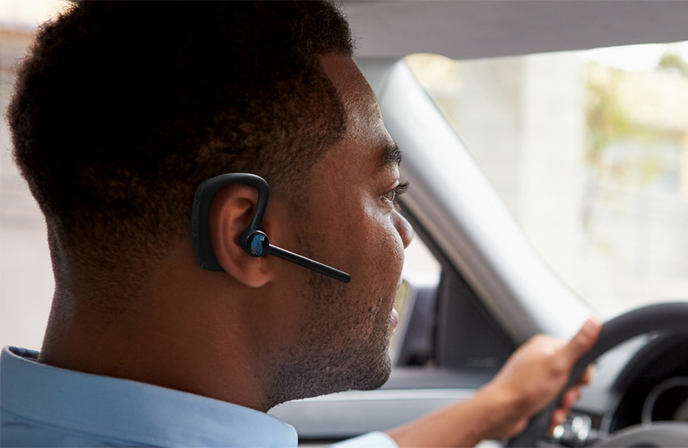 Rideshare driver inside car wearing BlueParrott M500-XT Bluetooth headset for hands-free communication.