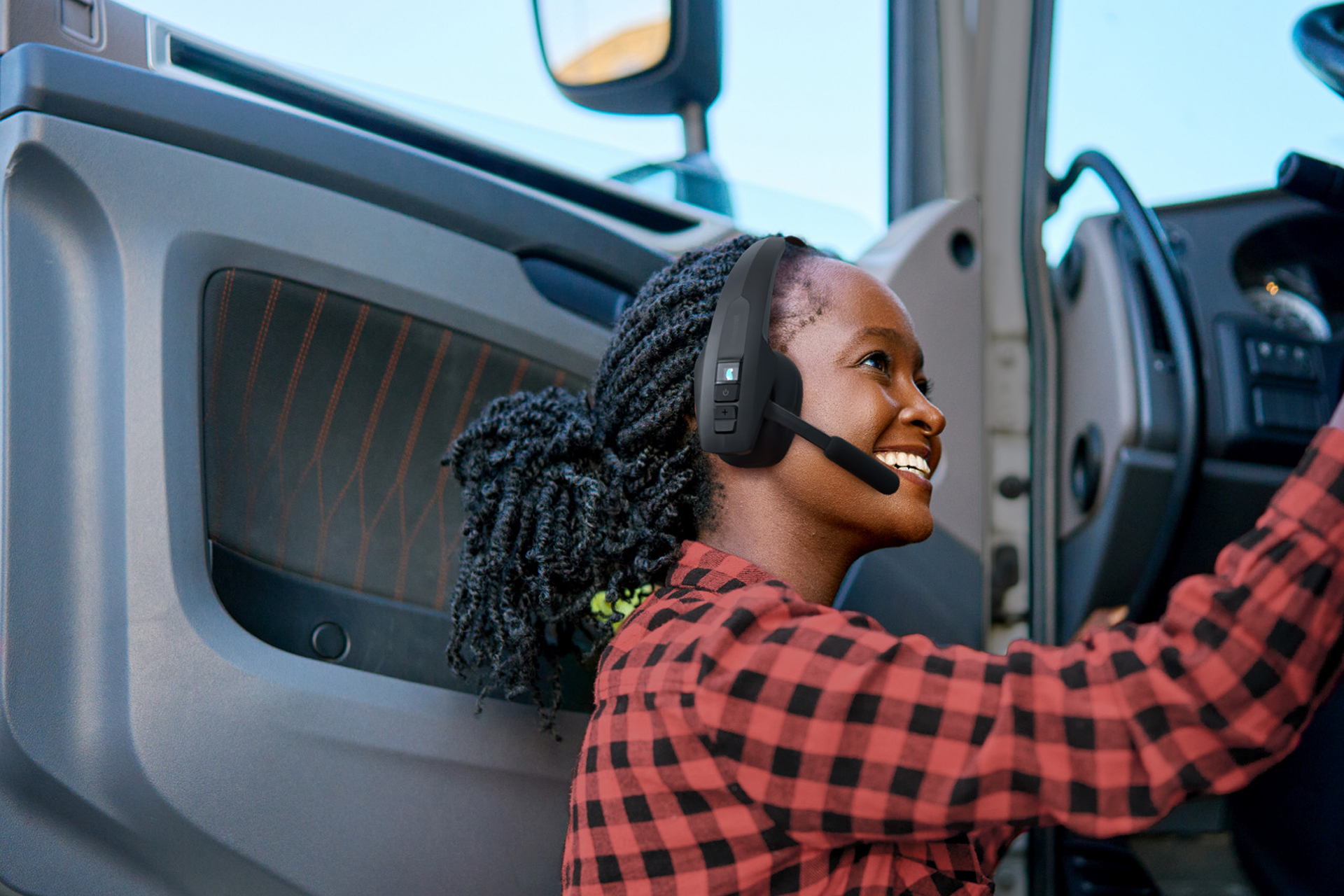 Professional truck driver wearing BlueParrott Pro B350 headset while climbing into a commercial vehicle cab, demonstrating hands-free communication for noisy on-the-road environments.